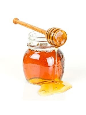Glass jar of golden honey with a wooden dipper, dripping with honey